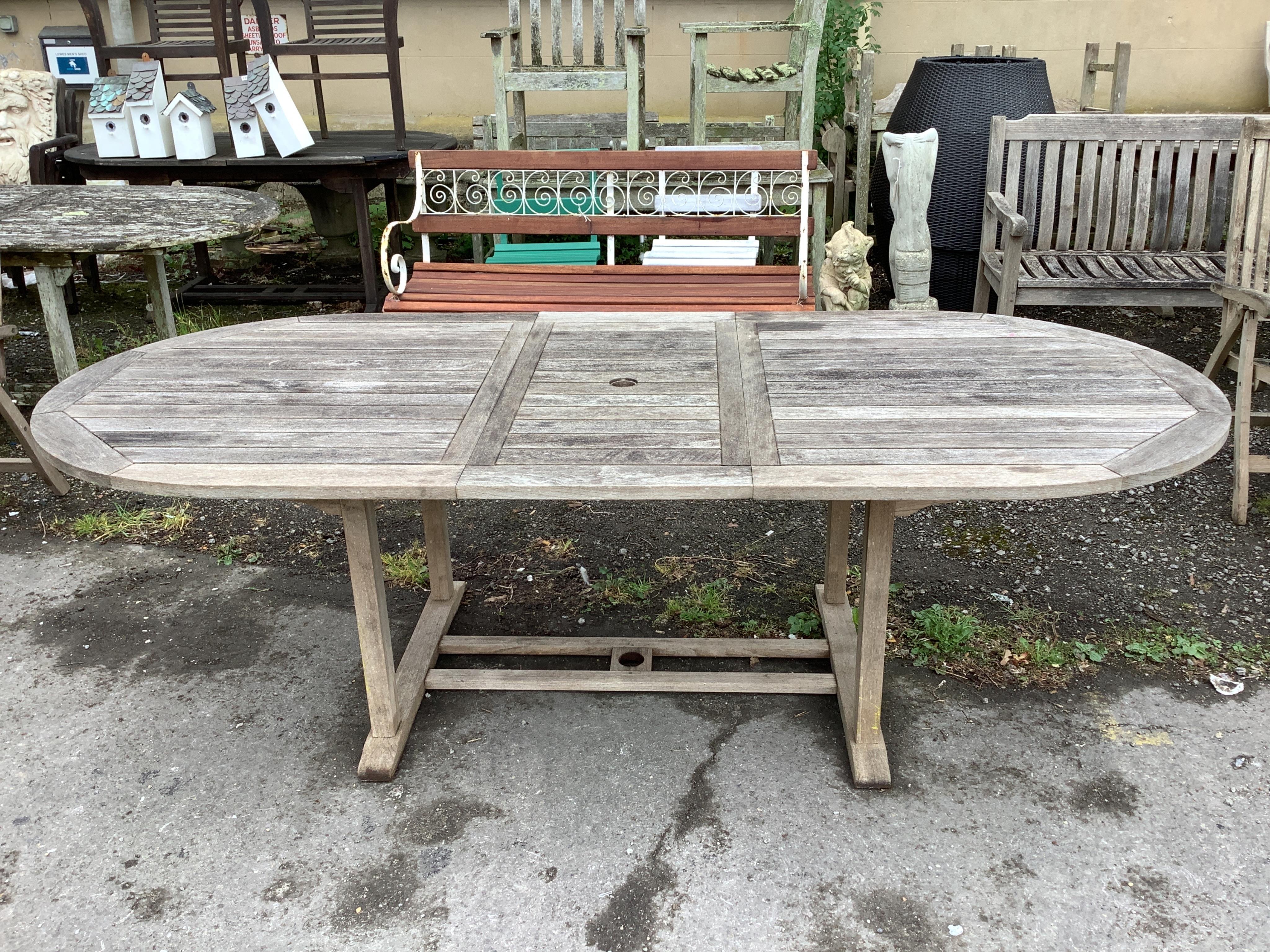 A weathered teak oval extending garden table, width 239cm extended, depth 109cm, height 73cm together with six Neptune weathered teak folding reclining garden armchairs with five Neptune cushions